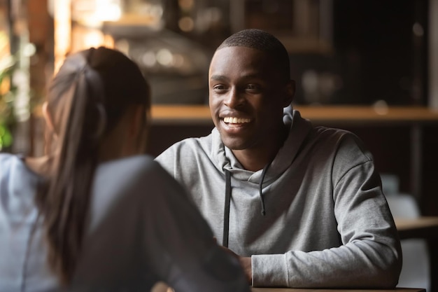 Vista traseira feminina sentada no local público do café foco em pessoas milenar interraciais masculinas africanas alegres que participam de busca de namoro rápido relacionamentos multirraciais e conceito de amor de alma gêmea