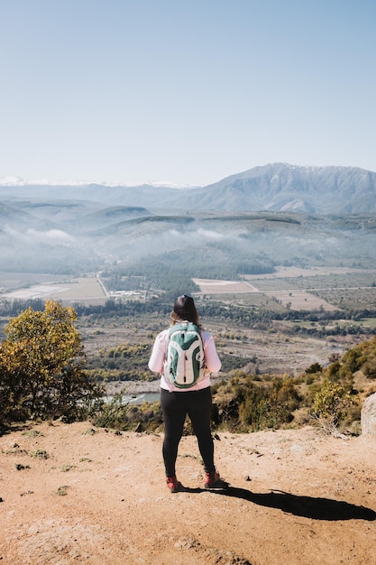 Vista traseira jovem latina plus size com mochila nas costas, contemplando a vista do topo de uma colina