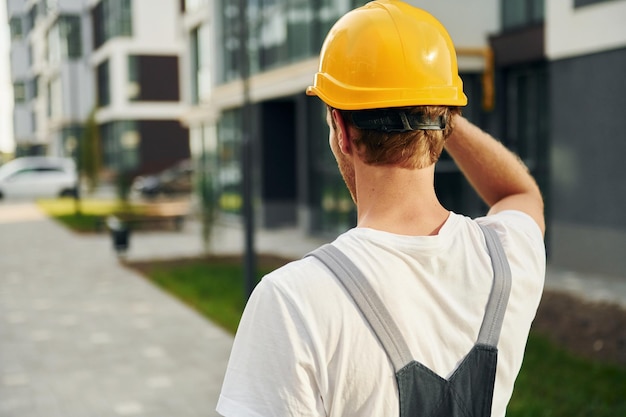 Vista traseira Jovem trabalhando de uniforme na construção durante o dia