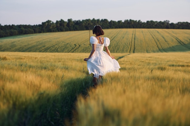 Vista traseira Linda jovem noiva de vestido branco está no campo agrícola em dia ensolarado