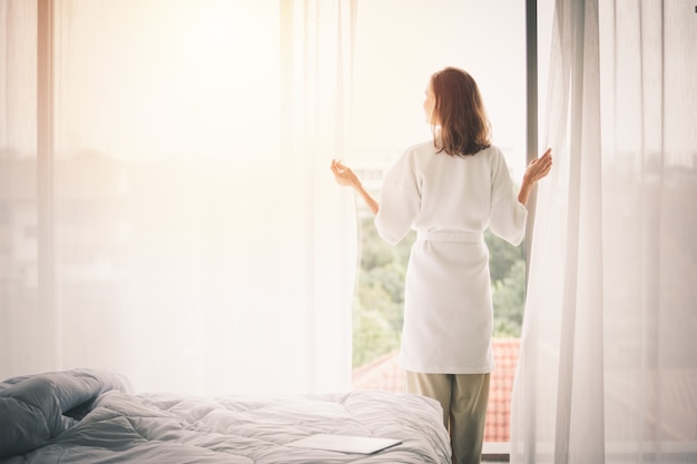 Vista traseira, mulher, abrindo cortinas, em, um, branca, quarto