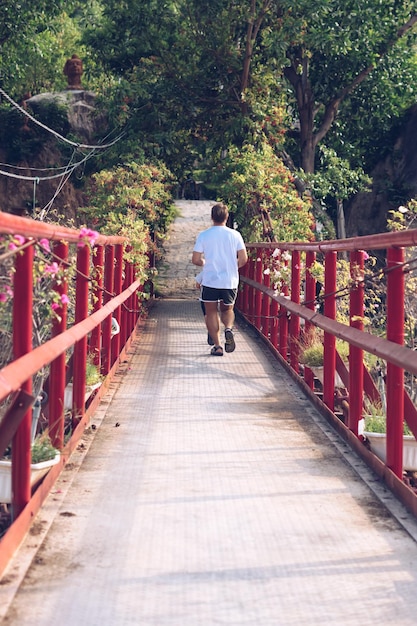Vista traseira O homem atravessa a ponte suspensa de ferro vermelho caminho para o parque florestal Esporte ao ar livre após a quarentena explorar o futuro da nova vida