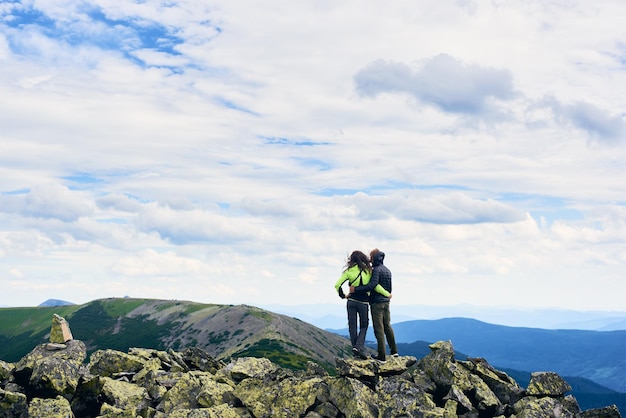 Vista traseira, os jovens estão abraçados em pedras no pico com belas vistas, vale das montanhas dos Cárpatos