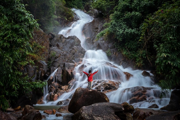 Vista traseira turista feminina em vestido vermelho em pé cachoeira na frente de sua paisagem natural