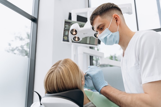 Vista traseira, um dentista examina os dentes de uma mulher atraente. Conceito de atendimento odontológico.