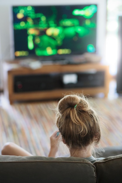 Vista trasera de una adolescente jugando a videojuegos en el sofá en casa