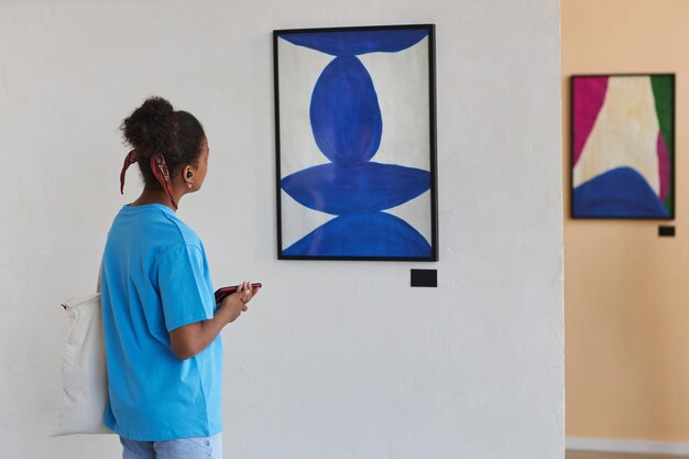 Vista trasera de una adolescente negra mirando arte abstracto en una galería de arte