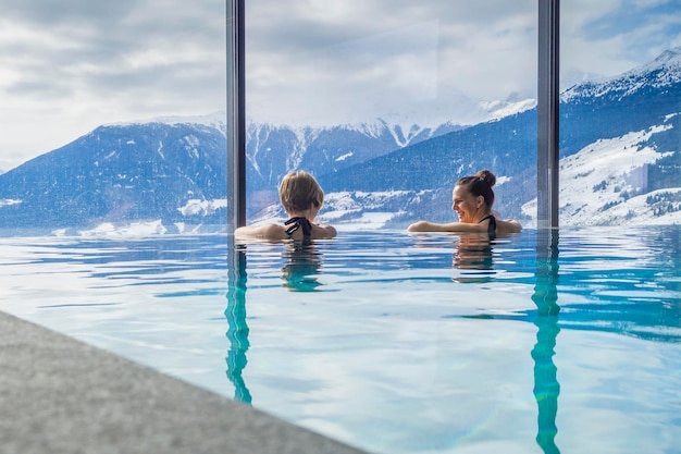 Vista trasera de amigas nadando en la piscina contra montañas cubiertas de nieve