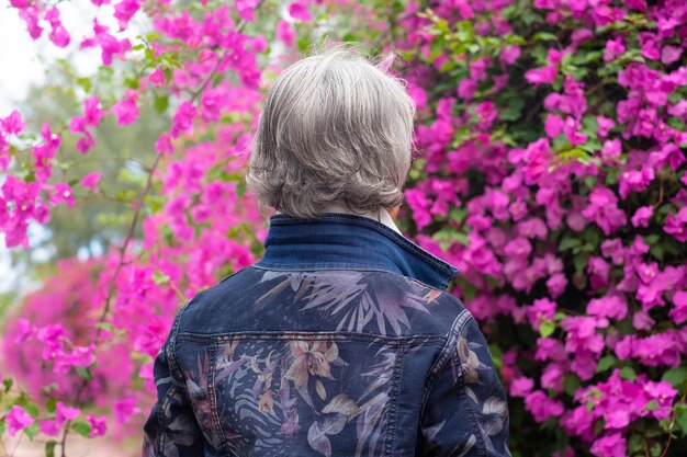 Vista trasera de una anciana en el parque admirando una buganvilla rosa floreciente Señora mayor de cabello blanco disfrutando de su tiempo libre y retiro al aire libre