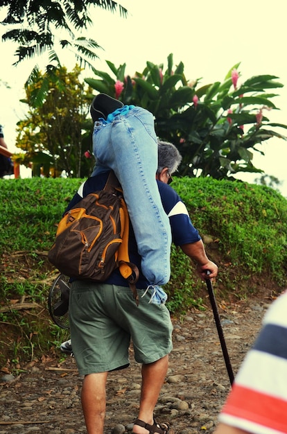 Foto vista trasera de un anciano con una mochila caminando por un camino de tierra