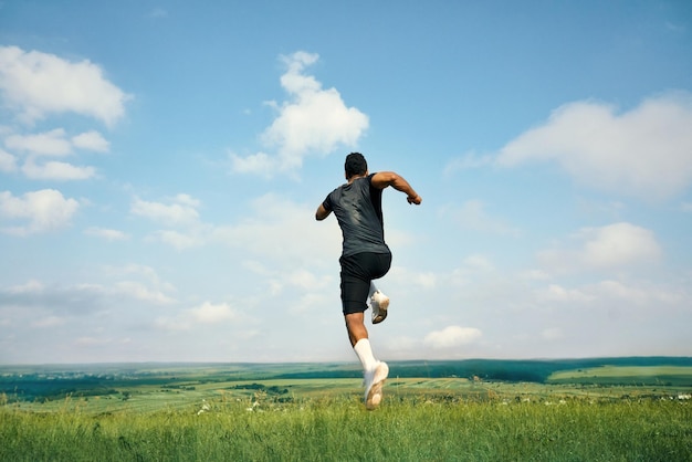 Vista trasera del atleta africano corriendo sobre hierba verde