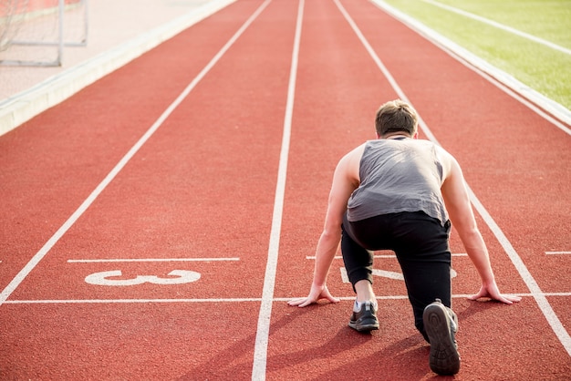 Foto vista trasera del atleta masculino listo para comenzar la carrera de relevos en la pista de atletismo