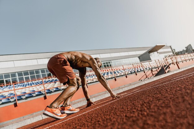 Vista trasera de un atleta preparándose para comenzar su sprint en una pista de atletismo para todo tipo de clima