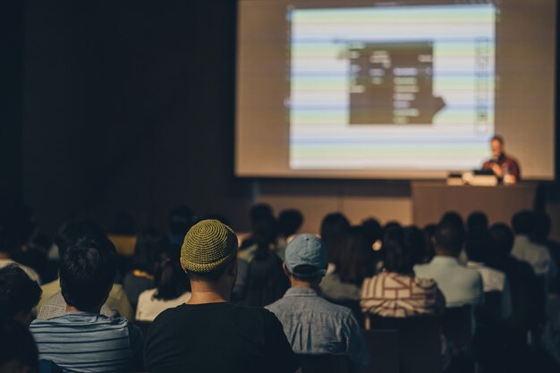 Vista trasera de la audiencia asiática que se une y escucha al orador hablando en el escenario del seminario