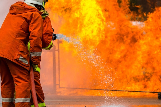 Foto vista trasera de un bombero rociando agua sobre el fuego mientras está de pie en la calle