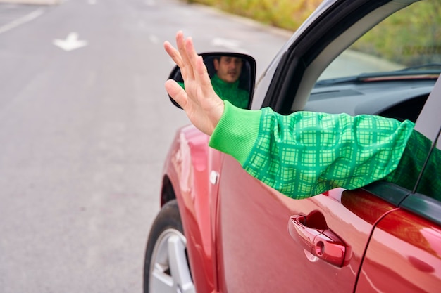 Vista trasera del brazo de un conductor saludando a alguien desde un automóvil en movimiento