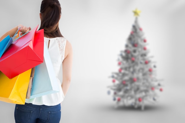 Foto vista trasera del cabello castaño sosteniendo bolsas de compras contra el árbol de navidad borroso en la habitación