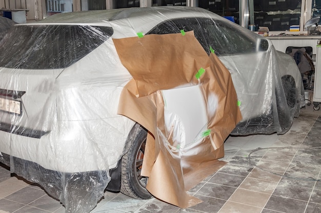 La vista trasera del camión después del accidente en la cámara para reparar la carrocería del camión está parcialmente cubierta con papel y pegada con cinta adhesiva verde para pintar la puerta lateral con blanco