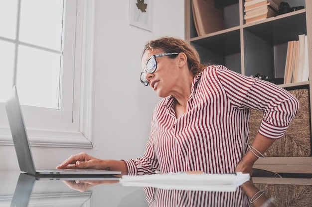 Vista trasera de cerca mujer joven estresada tocando la parte baja de la espalda sintiendo incomodidad que sufre de dolor repentino debido al estilo de vida sedentario o al exceso de trabajo de la computadora en una postura incorrecta en la oficina de casaxA