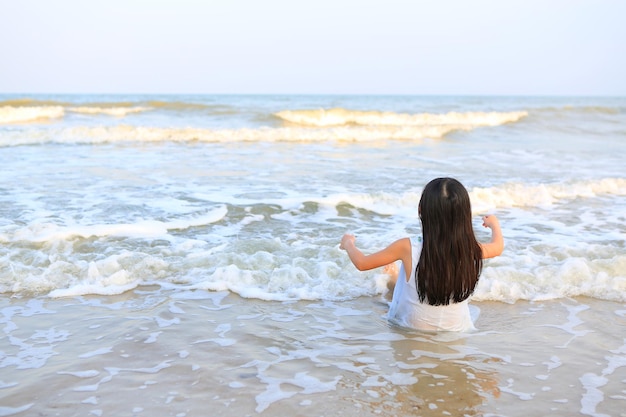 Vista trasera de una chica asiática sentada en la playa