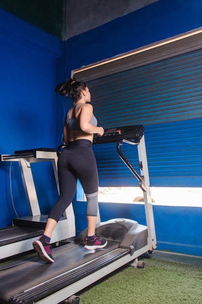 Vista trasera de una chica fitness corriendo en la cinta en el gimnasio.