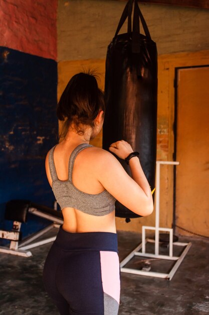 Vista trasera de una chica fitness lista para golpear el saco de boxeo.