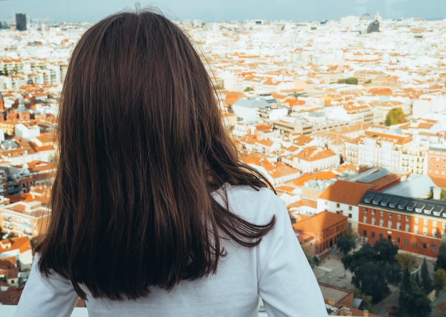 Vista trasera de una chica mirando el horizonte de la ciudad de Madrid desde la azotea de un edificio.