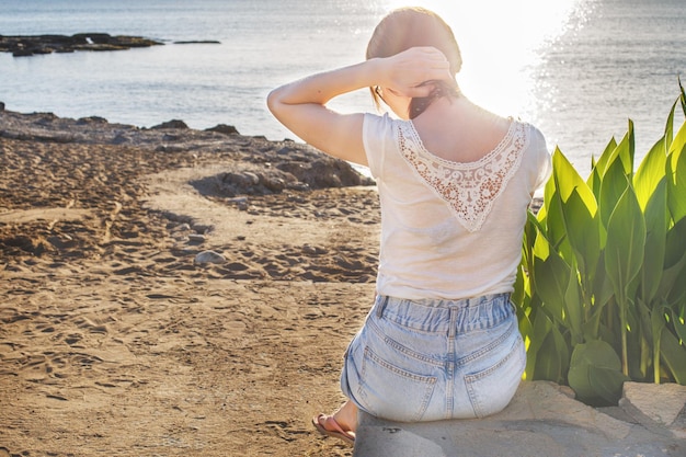 vista trasera de una chica sentada en la playa de arena sola en el fondo del mar