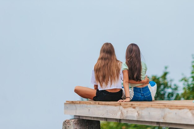 Foto vista trasera de chicas jóvenes sentadas en una terraza a una altura en las montañas contra el telón de fondo de la niebla y las montañas