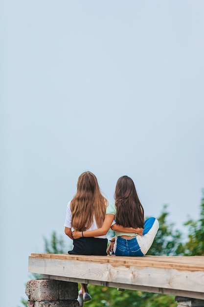 Foto vista trasera de chicas jóvenes sentadas en una terraza a una altura en las montañas contra el telón de fondo de la niebla