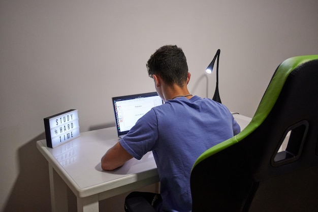 Una vista trasera de un chico que estudia con un letrero "estudiar tiempo difícil" en el escritorio