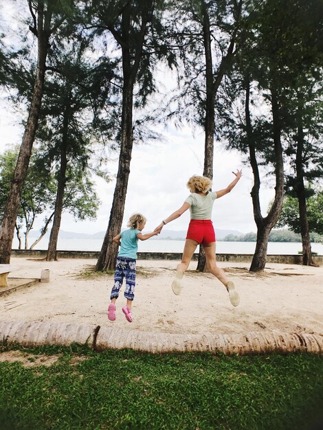 Foto vista trasera completa de la mujer y la hija saltando en la arena