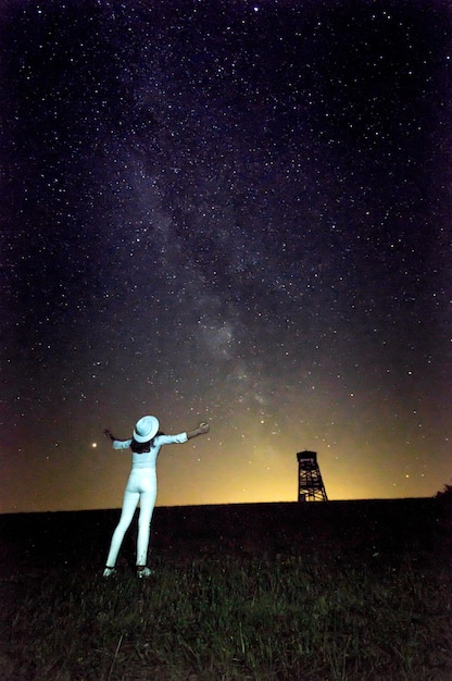 Foto vista trasera completa de la niña de pie contra el campo de estrellas por la noche