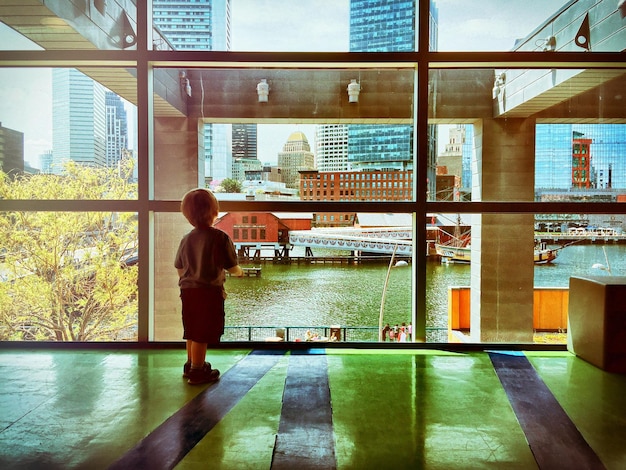 Foto vista trasera completa de un niño mirando a través de una ventana de vidrio en el museo de niños de boston