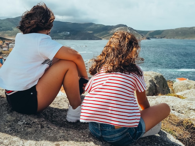 Vista trasera de dos chicas irreconocibles mirando un paisaje marino. Concepto tranquilo y silencioso.