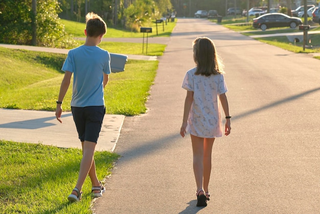 Vista trasera de dos jóvenes adolescentes, niña y niño, hermano y hermana caminando juntos en una calle suburbana en una tarde soleada