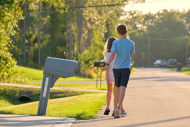 Vista trasera de dos jóvenes adolescentes, niña y niño, hermano y hermana caminando juntos en una calle suburbana en una tarde soleada
