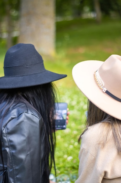 Vista trasera de dos niñas mirando la pantalla del teléfono Vista trasera de dos niñas con sombreros mirando la pantalla del teléfono celular Concepto de dos adolescentes mirando la pantalla del teléfono inteligente