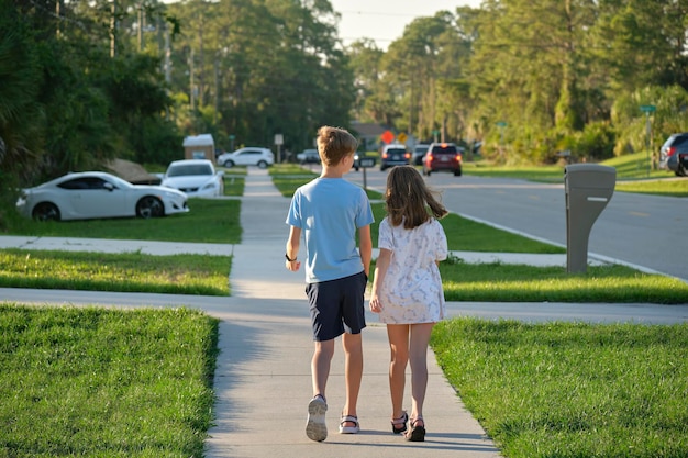 Vista trasera de dos niños adolescentes, niña y niño, hermano y hermana caminando juntos en una calle rural en un día soleado Concepto de tiempo de vacaciones