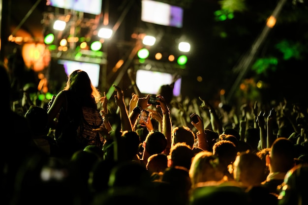 Vista trasera de emocionados fans animando un concierto de música y tomando fotos con sus teléfonos inteligentes