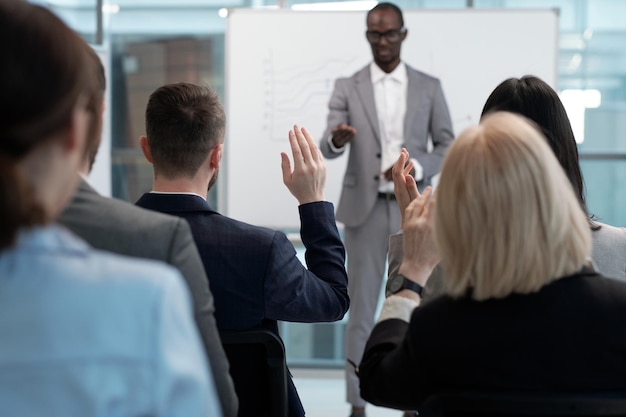 Vista trasera del empresario levantando la mano para responder preguntas entre colegas