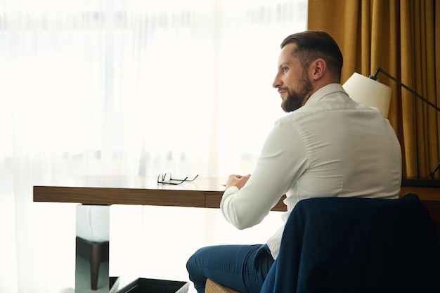 Vista trasera de un empresario de mediana edad sentado en una mesa en la habitación del hotel