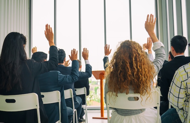 Vista trasera de empresarios casuales levantando la mano para hacer la pregunta sobre el evento educativo en un tablero