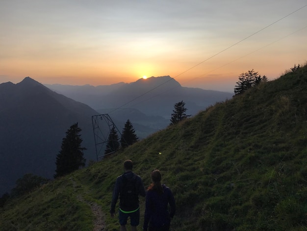Foto vista trasera de excursionistas caminando por la montaña contra el cielo durante la puesta de sol