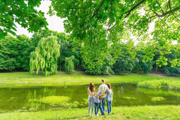 Vista trasera de la familia abrazándose mientras está de pie cerca del lago Los padres con dos hijos pasan tiempo al aire libre