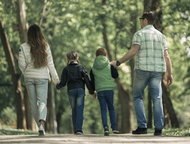 Vista trasera de la familia con dos niños caminando de la mano en el Parque el concepto de entretenimiento familiar