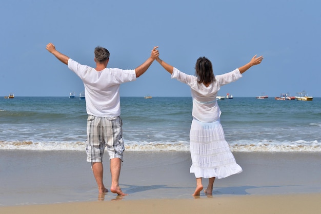 Vista trasera de la feliz pareja de pie en la orilla del mar con las manos levantadas