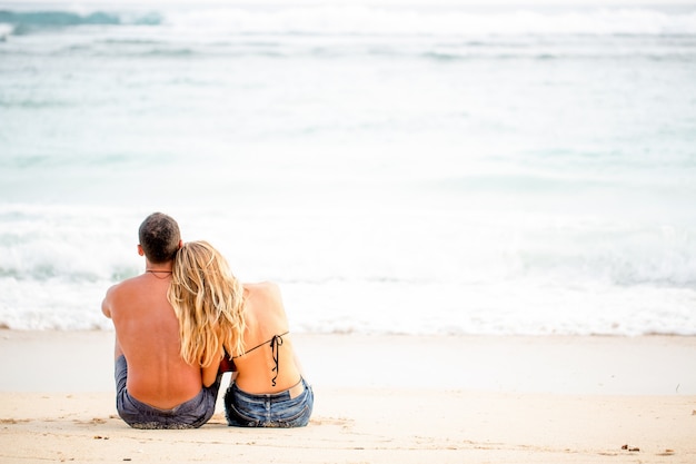 Vista trasera de la feliz pareja sentada en la costa