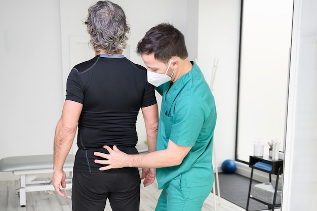 Vista trasera de un fisioterapeuta examinando la espalda del hombre.