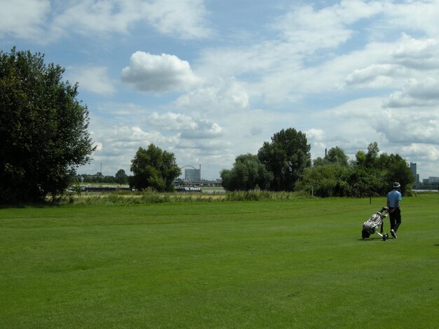 Foto vista trasera de un golfista tirando de una bolsa de golf en curso contra el cielo